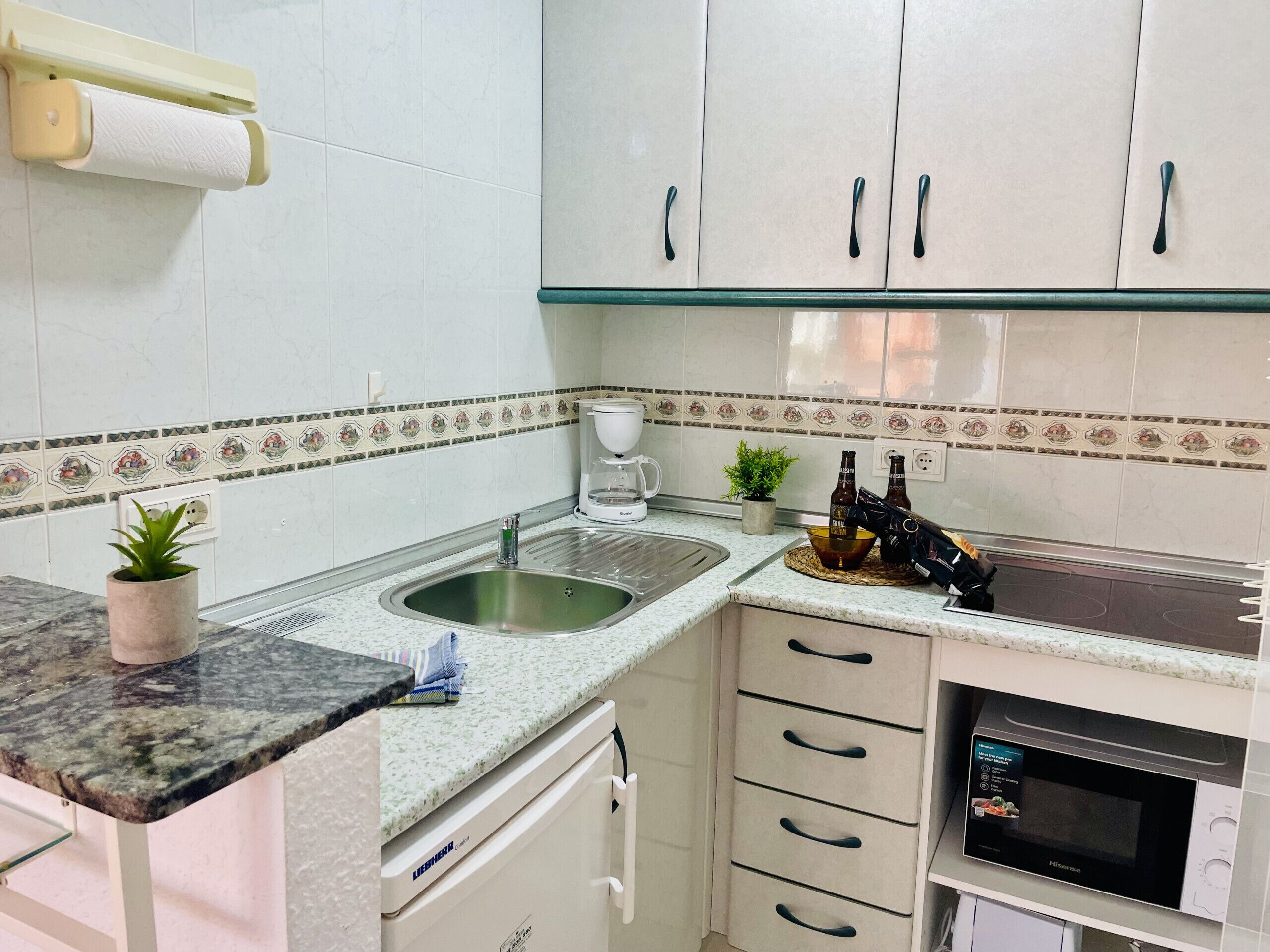Una cocina con un lavamanos, una cafetera, un microondas y armarios.
