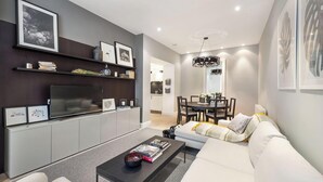 A modern living room with a sofa, coffee table, and TV. There is a dining area with a table and chairs. - Pavilion Road Mews House - 4 bed (London)