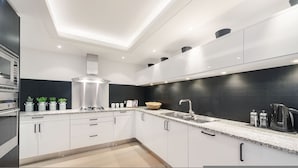 A modern kitchen with white cabinets, a stainless steel range hood, a black backsplash, and a granite countertop. - Pavilion Road Mews House - 4 bed (London)