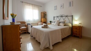 Une chambre à coucher comprenant un lit, des tables de chevet, une commode, une chaise, une fenêtre avec des rideaux et des éléments de décoration murale.