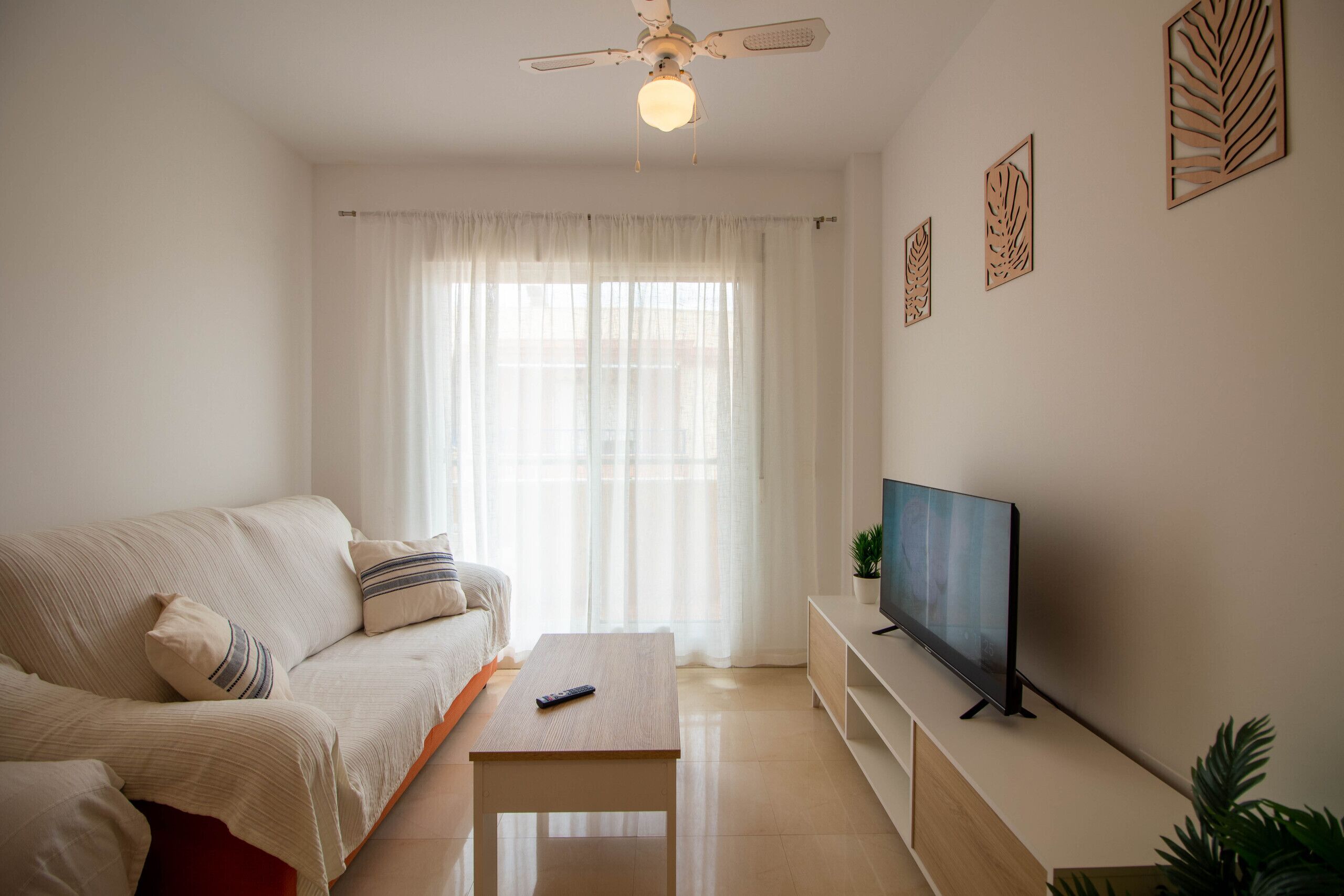 Un salon comprenant un canapé, une table basse, un téléviseur posé sur un meuble et un ventilateur de plafond.