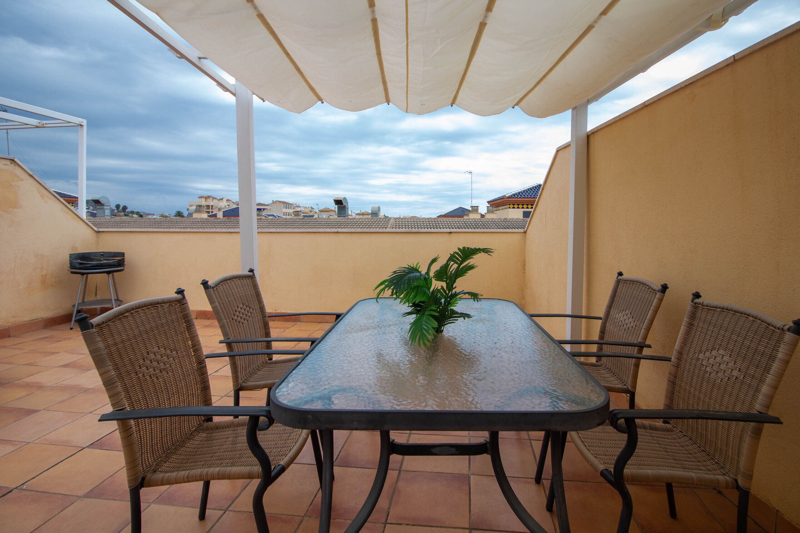 Une terrasse avec une table et des chaises, une plante en pot et un parasol blanc.