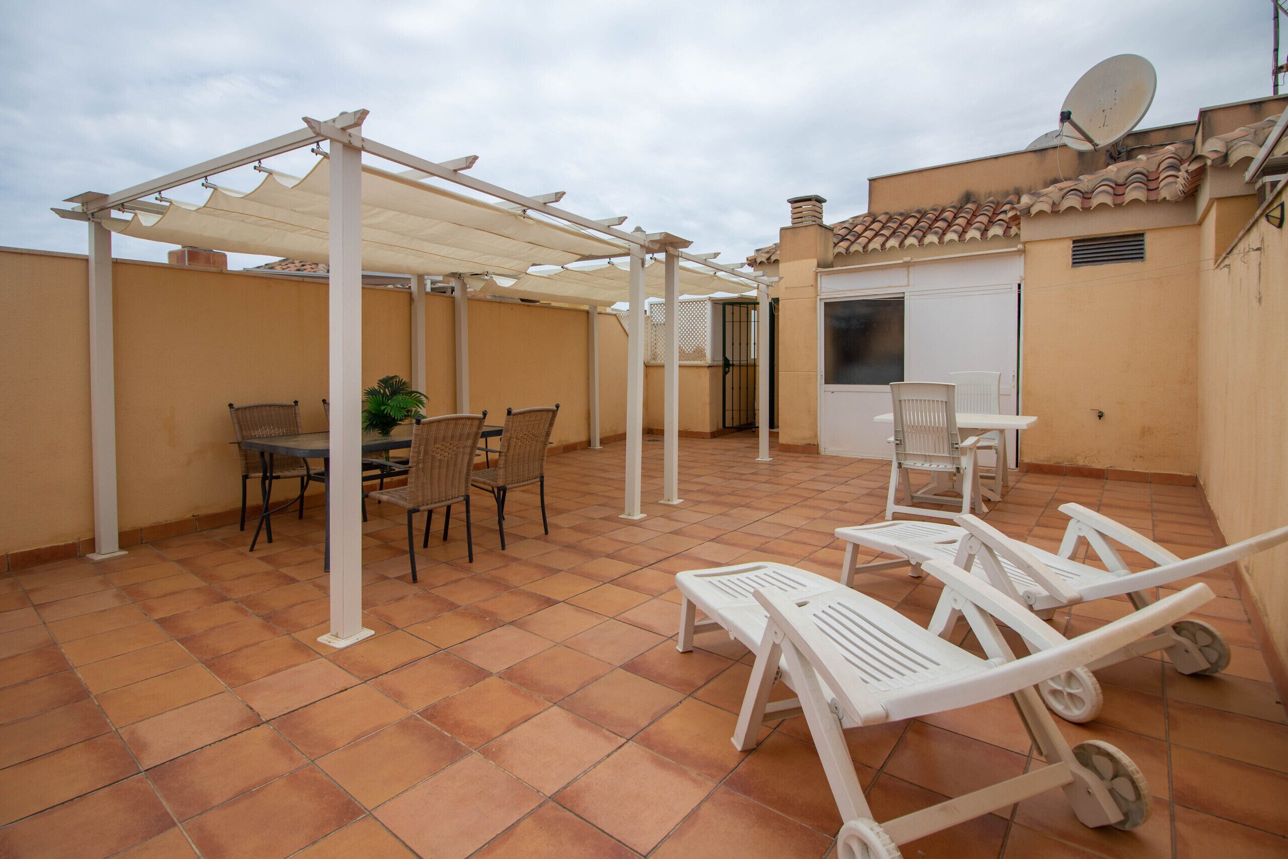 A covered patio with a table and chairs, a white umbrella, and a white chair with wheels.