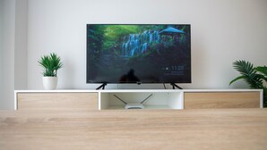 A flat-screen TV on a white TV stand with a waterfall wallpaper, a potted plant on the left, and a potted plant on the right. - Andaluc a Sun Duplex Torrox-costa (Torrox)