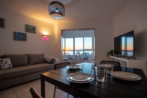 Un comedor con una mesa preparada para dos personas, un sofá y un televisor sobre un mueble.