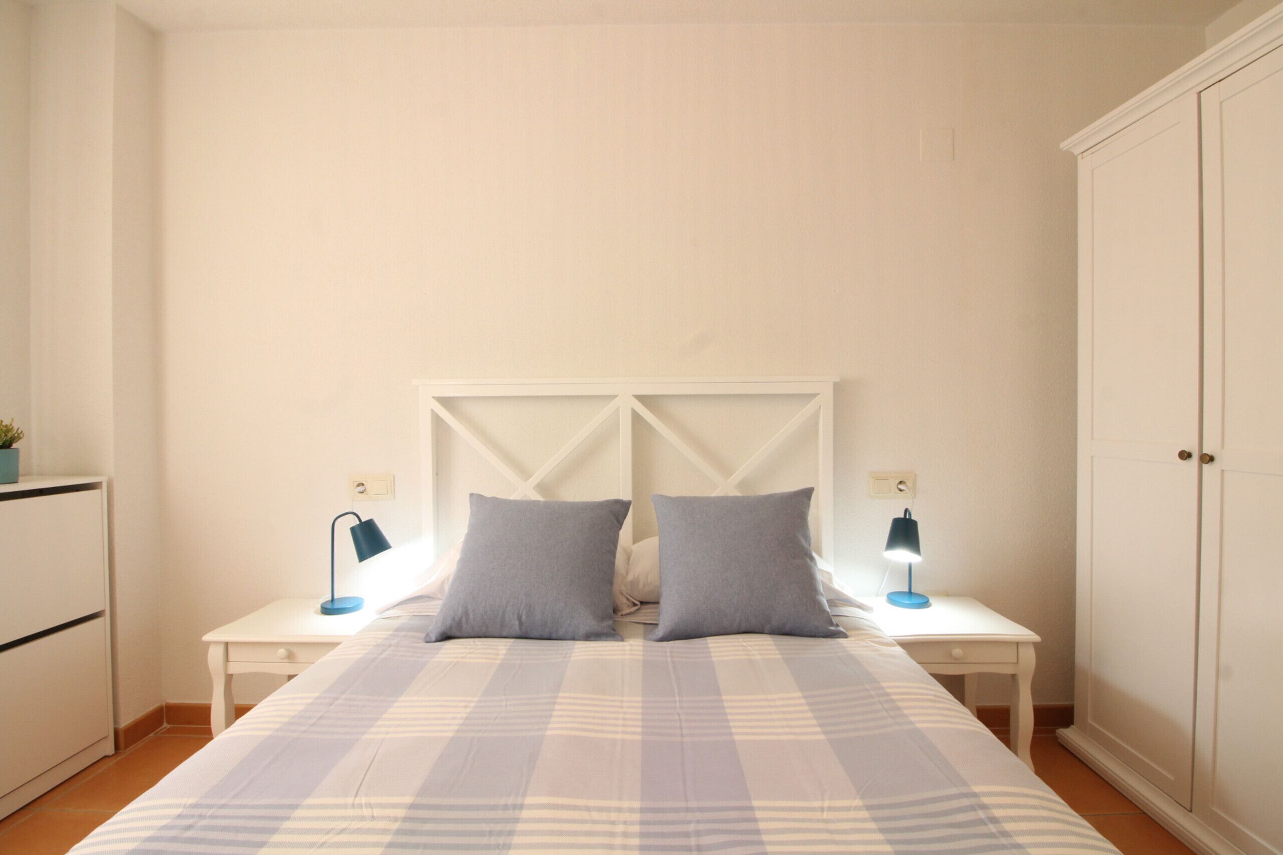 A bedroom with a bed, two bedside tables with lamps, a wardrobe, and a small desk with a lamp.