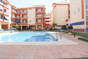 A swimming pool surrounded by multi-story buildings with balconies, a clear sky, and potted plants. - Carpe Diem by At Home Costa del Sol (Torrox)