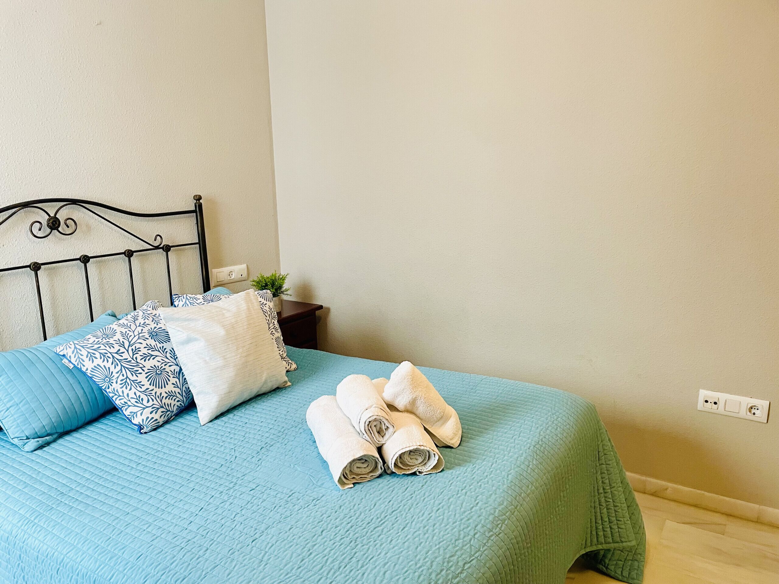 A bed with a blue quilt, two patterned pillows, and rolled towels.