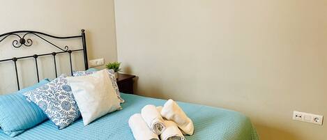 A bed with a blue quilt, two patterned pillows, and rolled towels.