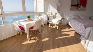 Une pièce comprenant une table à manger, des chaises, un lit, une table de chevet, une lampe, une bibliothèque et une vue sur la mer.