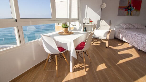 Une pièce comprenant une table à manger, des chaises, un lit, une table de chevet, une lampe et une vue sur la mer.