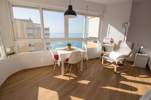A room with a dining table, chairs, a sofa, a small bedside table, a lamp, and a view of the sea. - Madrid del Mar Viii Torrox Costa (Torrox)