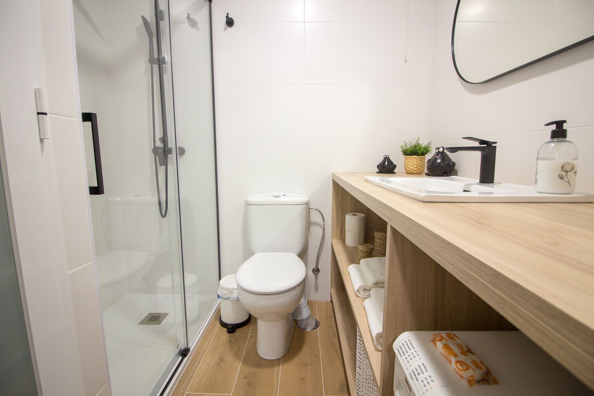 Une salle de bain moderne avec une douche à parois de verre, des toilettes, un lavabo doté d’un plan de travail en bois et un miroir.