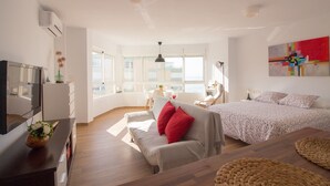 Une chambre moderne avec un lit, un canapé, une télévision et une grande fenêtre.
