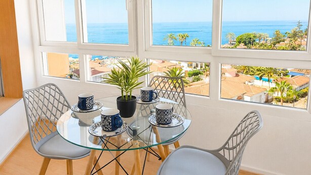 Een balkon met een glazen tafel, stoelen en een plant in pot.