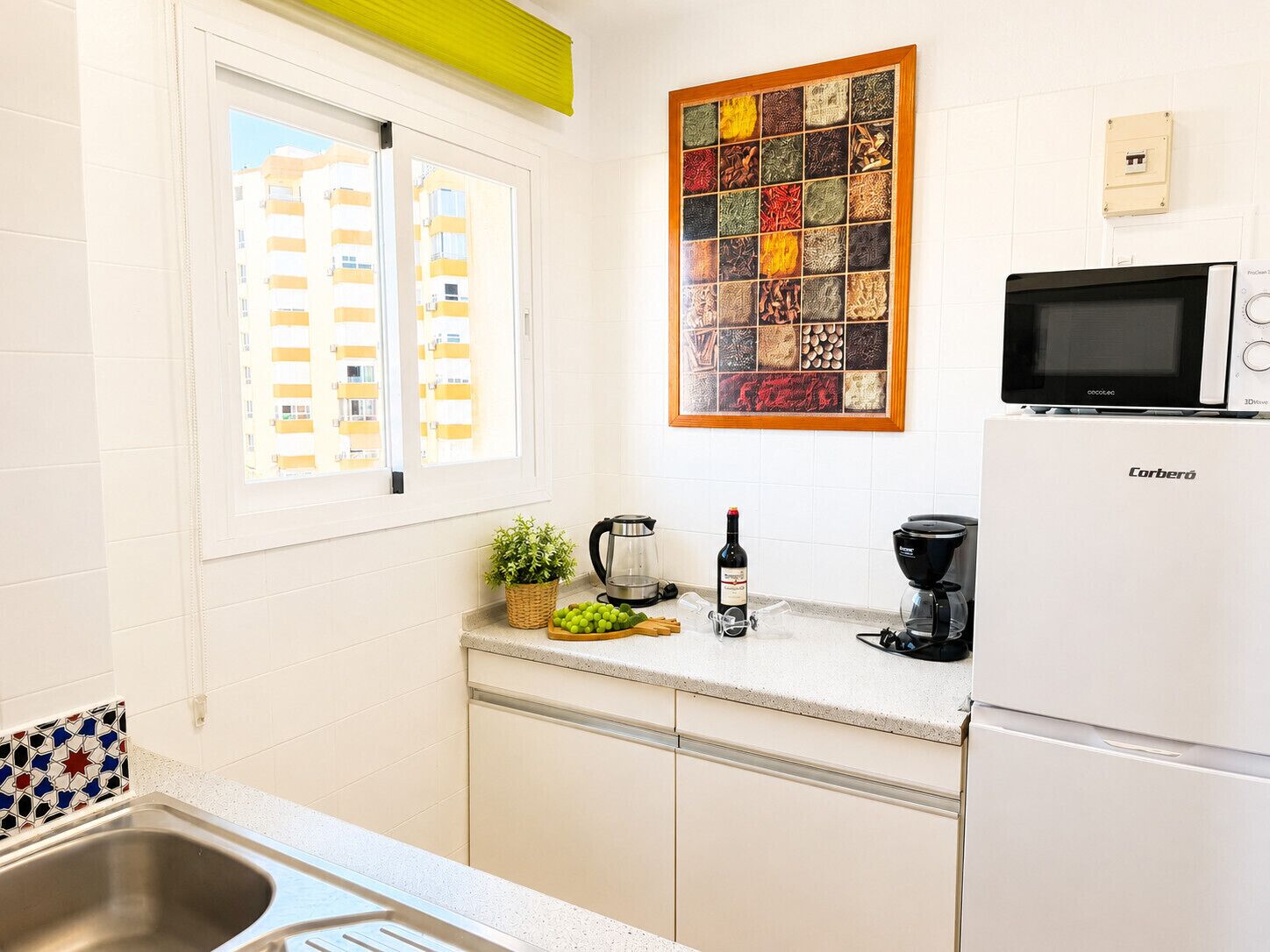 A kitchen with a refrigerator, a microwave, a coffee maker, and a wine bottle.