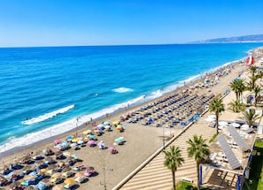 A beach with rows of sun loungers and umbrellas, a clear blue sea, and a distant shoreline. - Madrid 401 by At Home Costa del Sol (Torrox)