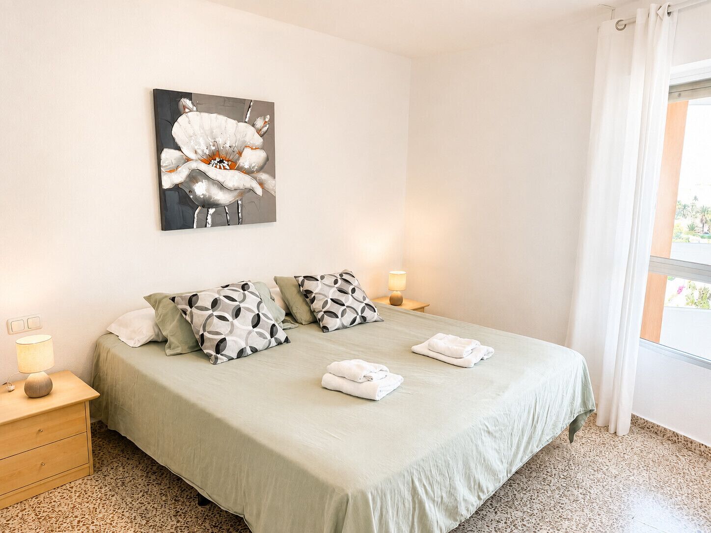 A hotel room with a bed, pillows, a nightstand, a lamp, and a painting on the wall.