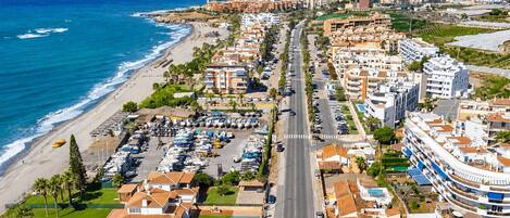 Vue aérienne d’une ville côtière avec une plage, une route principale et des immeubles résidentiels.