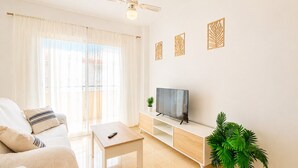 Een woonkamer met een bank, een salontafel, een tv op een meubelstuk, een plafondventilator en een plant.