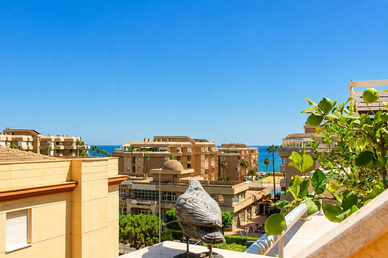 A coastal cityscape with buildings, a clear sky, and a statue.