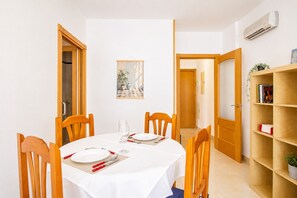 A dining area with a round table, wooden chairs, a white tablecloth, and a bookshelf with books and a plant. - Andalusia Sun Duplex | Torrox-Costa (Torrox)