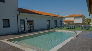 Una piscina con solárium empedrado, un edificio con tejado de baldosas y una fila de sillones de descanso.