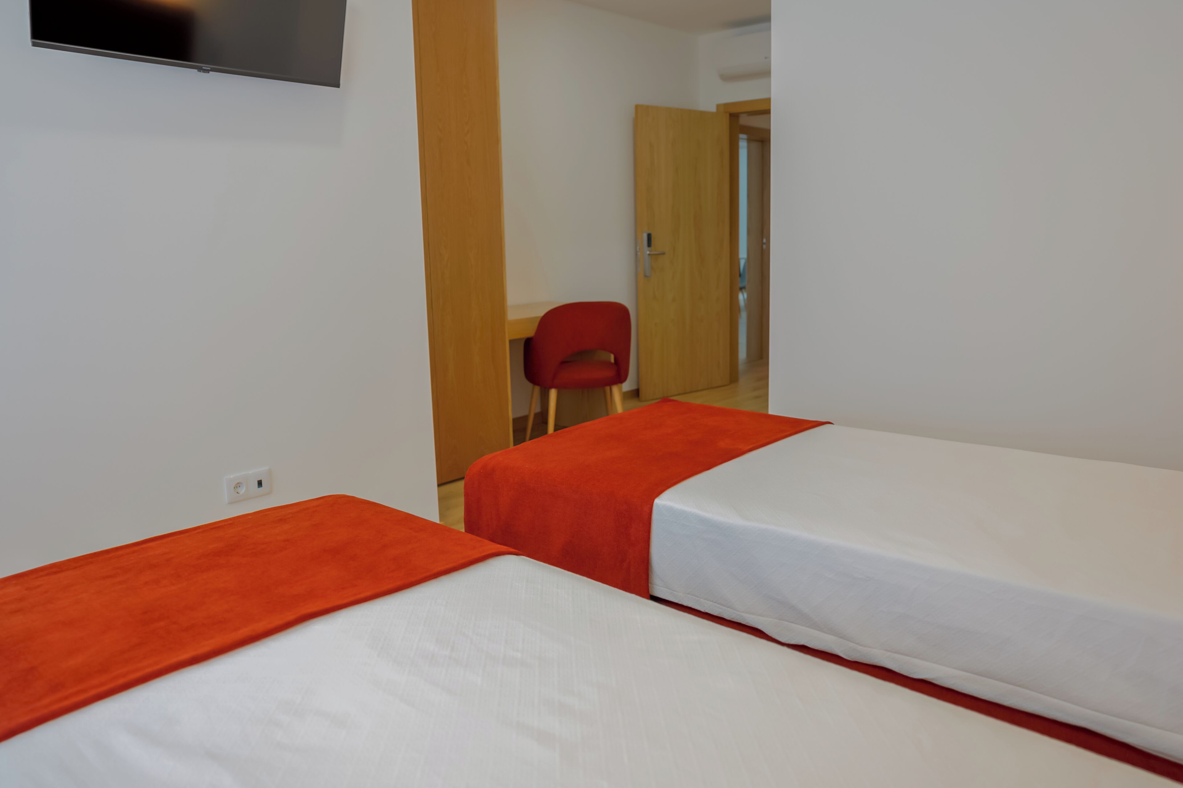 A hotel room with two beds, a television mounted on the wall, and a wooden door in the background.