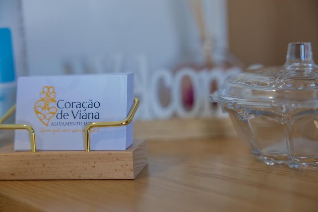 A business card for 'Coracao de Viana' on a wooden stand with a clear glass container nearby.