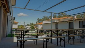 Un patio al aire libre con varias mesas y bancos de madera, cielo despejado y edificios residenciales al fondo.