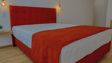 Un letto con una testiera rossa e biancheria bianca, una pianta sul comodino e due lampadine fissate al muro.