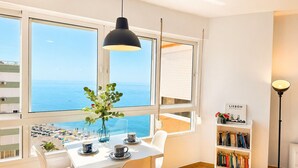 Een kamer met een gedekte tafel voor twee personen, een boekenkast en uitzicht op zee door grote ramen.