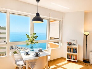 A room with a table set for two, a bookshelf, and a view of the sea through large windows. - Madrid 810 by At Home Costa del Sol (Torrox)