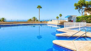 Une piscine avec des marches permettant d’y accéder, entourée de palmiers et offrant une vue sur l’océan.