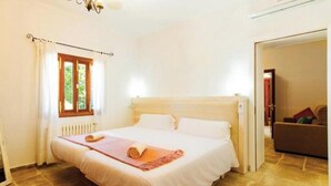 Ein Schlafzimmer mit Bett, einem Fenster mit Vorhängen, einem Heizkörper und einer Tür zu einem anderen Raum.