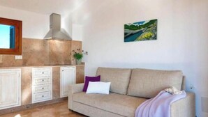 Ein Wohnzimmer mit Sofa, einem Bild an der Wand und einer Küchenzeile inklusive Schränke und Herd.