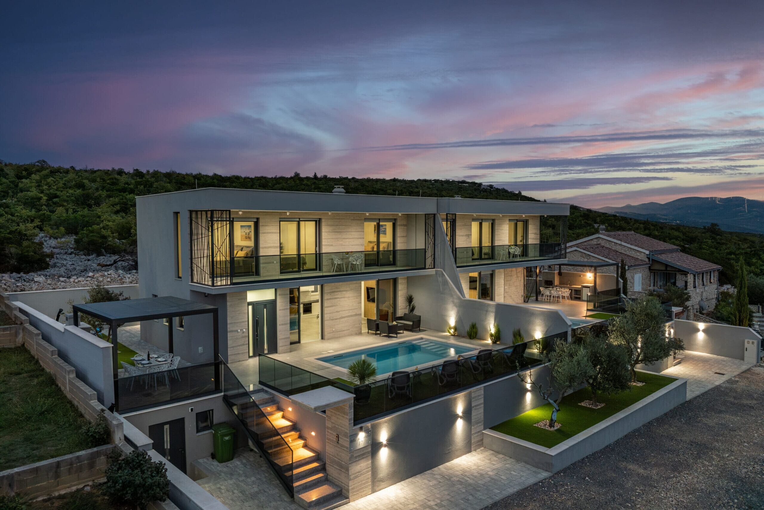 Una casa moderna de dos pisos con piscina, mobiliario exterior y una escalera que lleva al nivel superior.