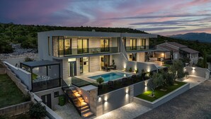 Una casa moderna de dos pisos con piscina, mobiliario exterior y una escalera que lleva al nivel superior.