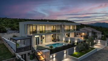 Una casa moderna de dos pisos con piscina, mobiliario exterior y una escalera que lleva al nivel superior.