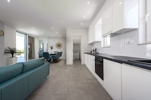 A modern kitchen with white cabinets, a black countertop, and a dining area with a teal sofa and chairs.