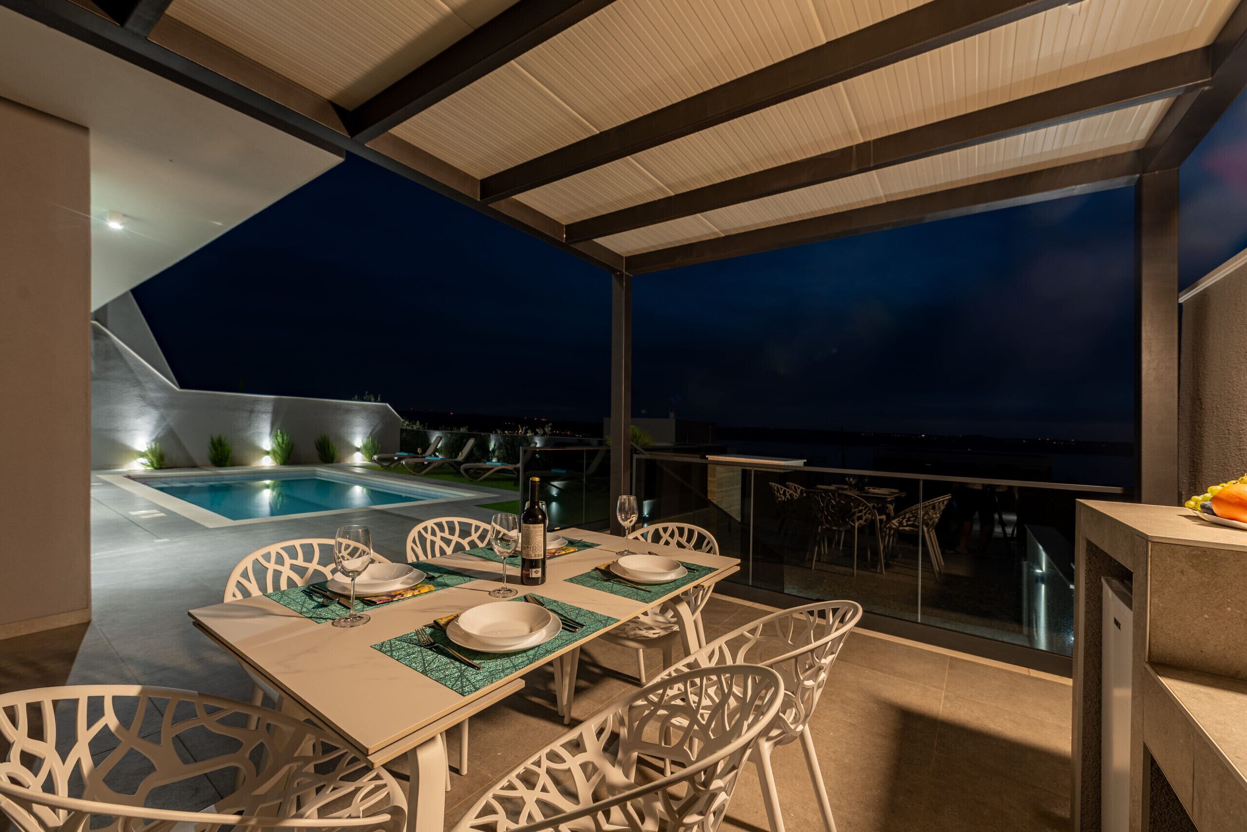 A dining area with a pool view, white chairs, and a table set for two.