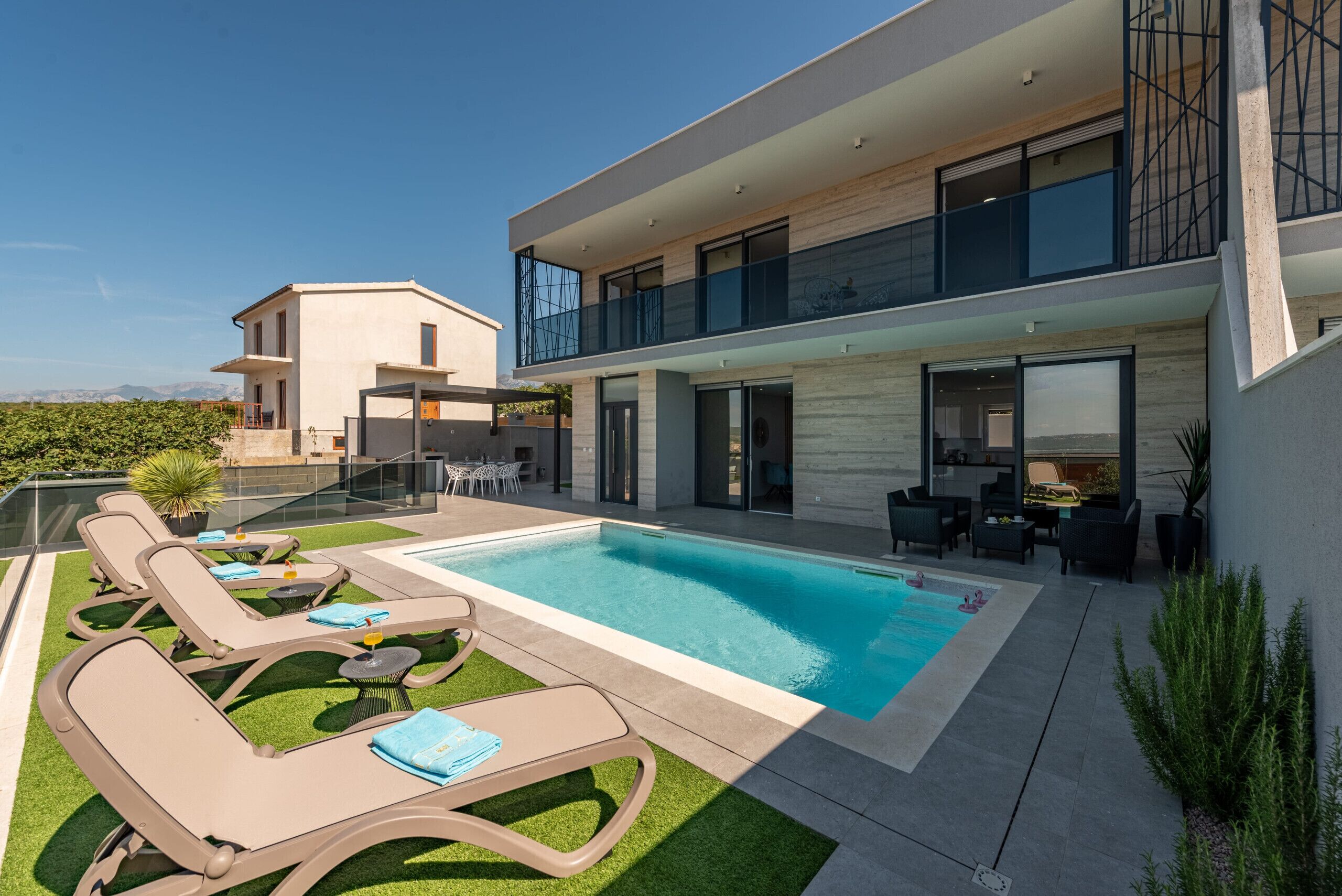 Una casa moderna de dos pisos con piscina, mobiliario exterior y un balcón.