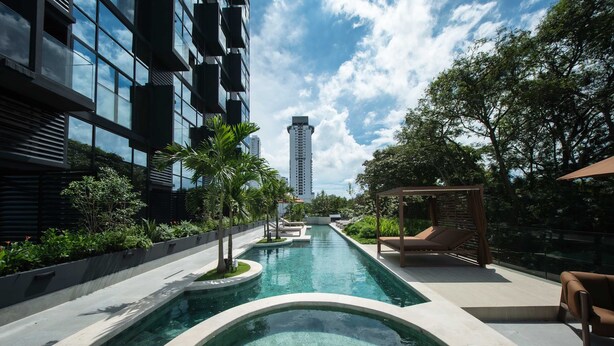 Piscina com design moderno, rodeada por vegetação e um edifício com grandes janelas.