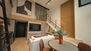 Um espaço de estar moderno com televisão de tela plana, uma escada, uma sala de jantar com mesa redonda e um sofá.