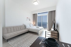 A modern hotel room with a sofa, a bed, a dining table, and a view of the city. - Free Housekeeping Visits During Your Stay - Stayshort - Majestic Studio in Bloom Tower C Perfect for 3 (Dubai)
