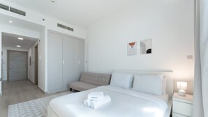 A modern hotel room with a large bed, a sofa, a nightstand with a lamp, and a wardrobe. - Free Housekeeping Visits During Your Stay - Stayshort - Majestic Studio in Bloom Tower C Perfect for 3 (Dubai)