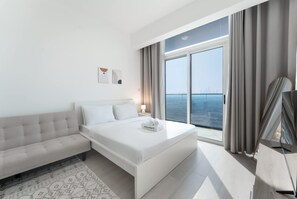 A modern hotel room with a large bed, a sofa, a TV, and a view of the city. - Free Housekeeping Visits During Your Stay - Stayshort - Majestic Studio in Bloom Tower C Perfect for 3 (Dubai)