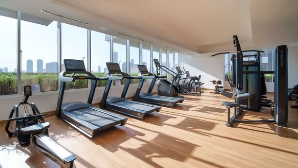 A modern gym with treadmills, elliptical machines, and weight equipment. Large windows offer a city view. - Free Housekeeping Visits During Your Stay - Stayshort - Majestic Studio in Bloom Tower C Perfect for 3 (Dubai)