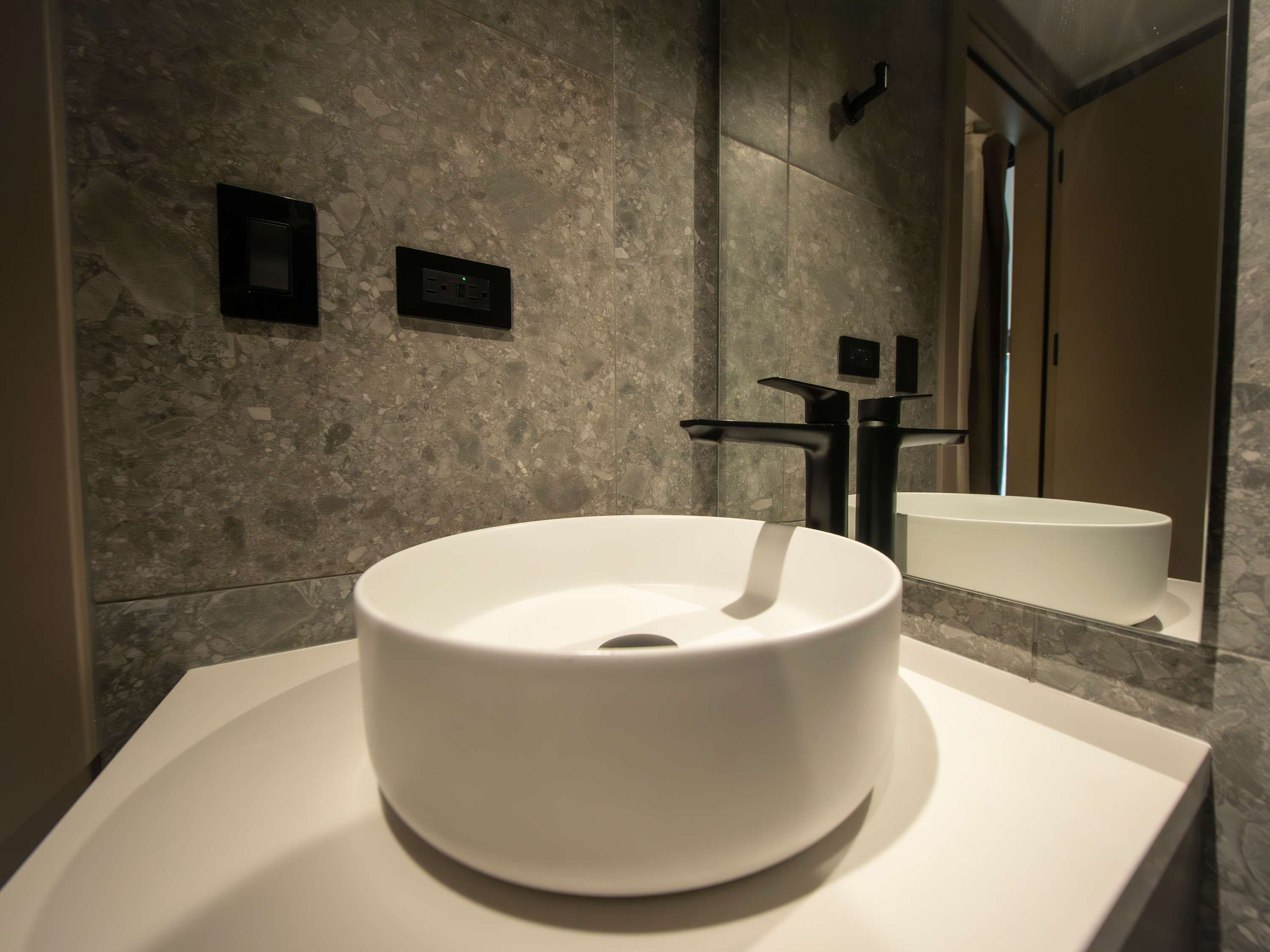 A modern bathroom with a round white sink, a black faucet, and a marble wall.