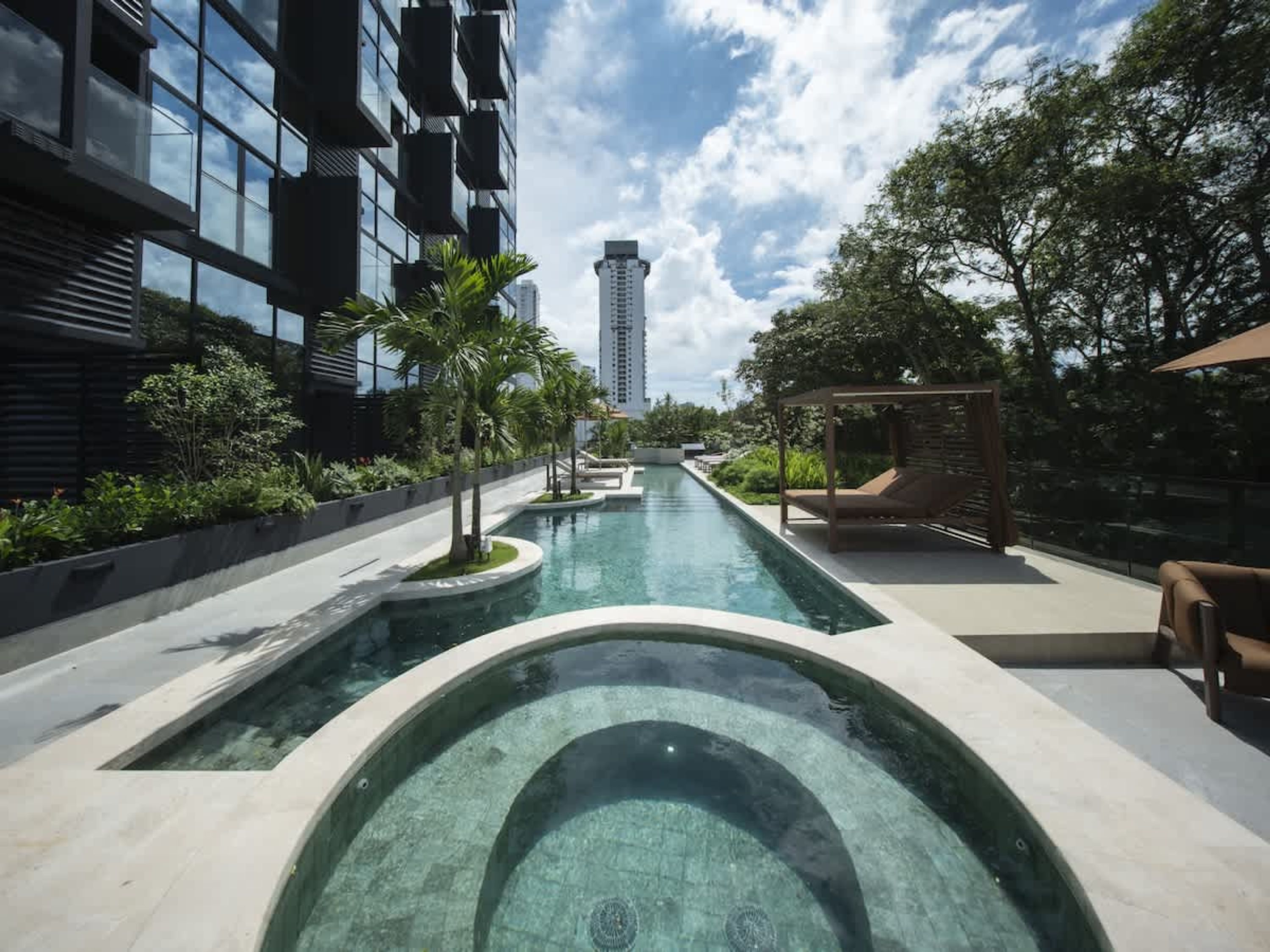 Une piscine au design moderne, entourée de verdure et bordée d’un bâtiment doté de grandes fenêtres.